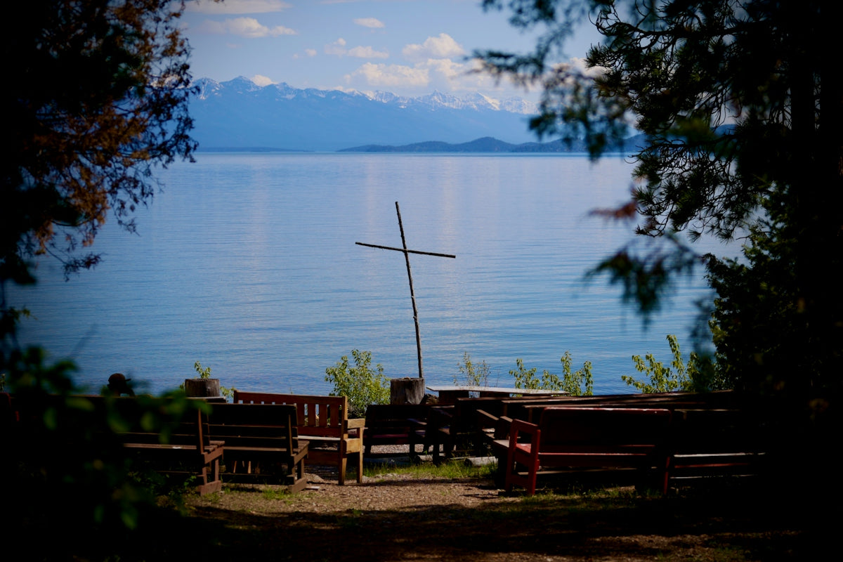 A rustic cross and benches by a lake with mountains