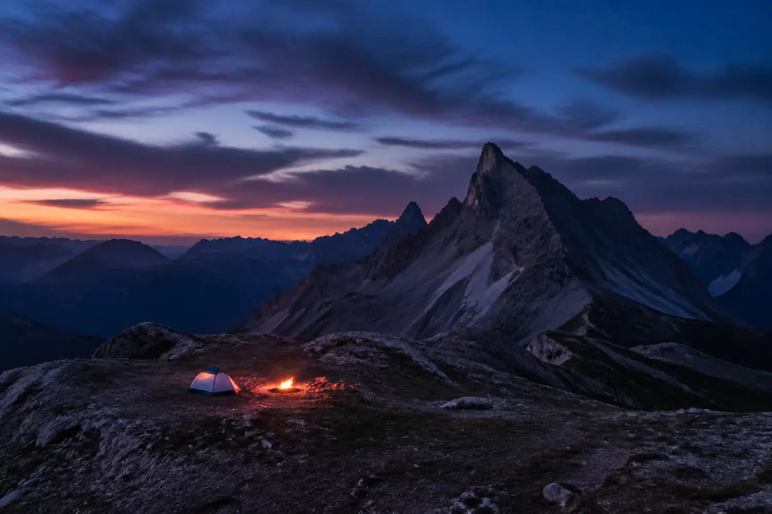 A glowing campfire and tent under a rugged mountain peak at twilight, reflecting peaceful spiritual adventure.
